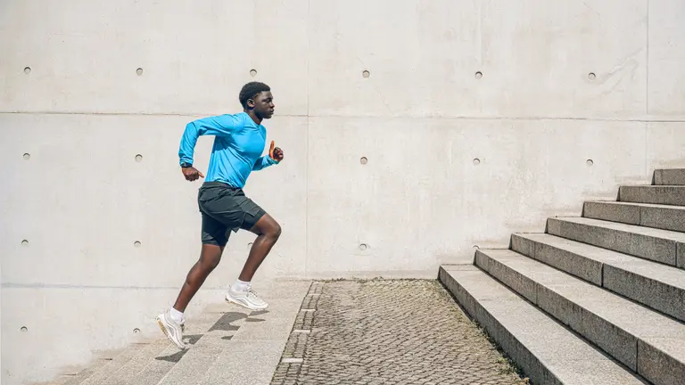 Young sportsman running up steps in front of concrete wall outdoors at sunny day.