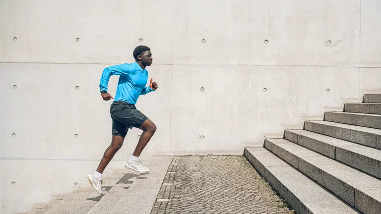 Young sportsman running up steps in front of concrete wall outdoors at sunny day.